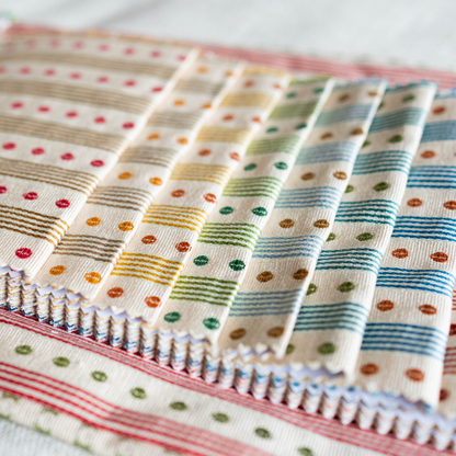 Stack of patterned fabric swatches . Domino Stripe by Manuel Canovas in different colors. 