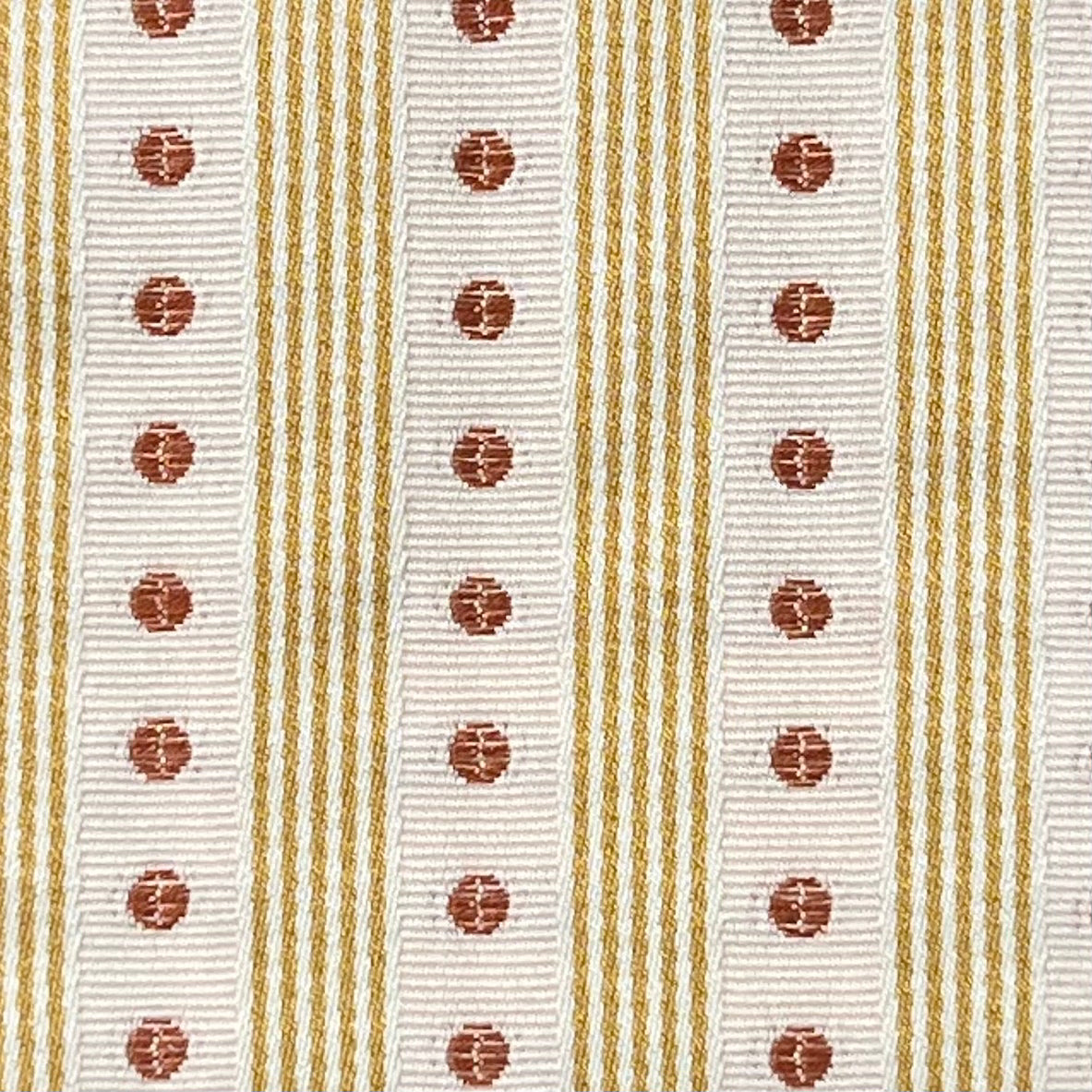 Close-up of a ribbon with white background, gold stripes, and red circular patterns. Manuel Canovas fabric.
