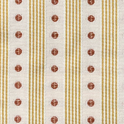 Close-up of a ribbon with white background, gold stripes, and red circular patterns. Manuel Canovas fabric.