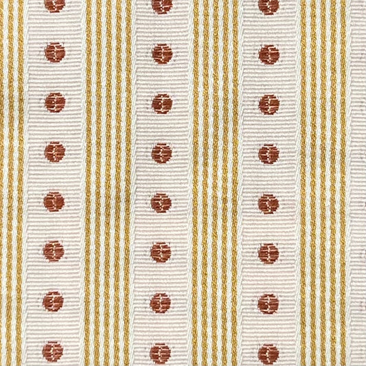 Close-up of a ribbon with white background, gold stripes, and red circular patterns. Manuel Canovas fabric.
